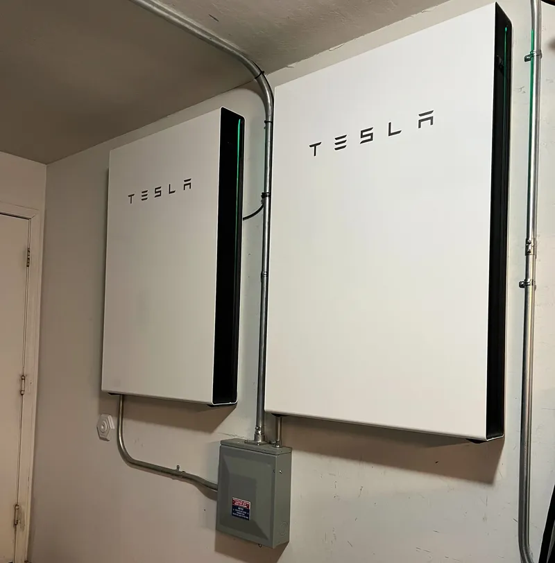 Two white Tesla Powerwall home batteries mounted on an interior residential wall with conduit.