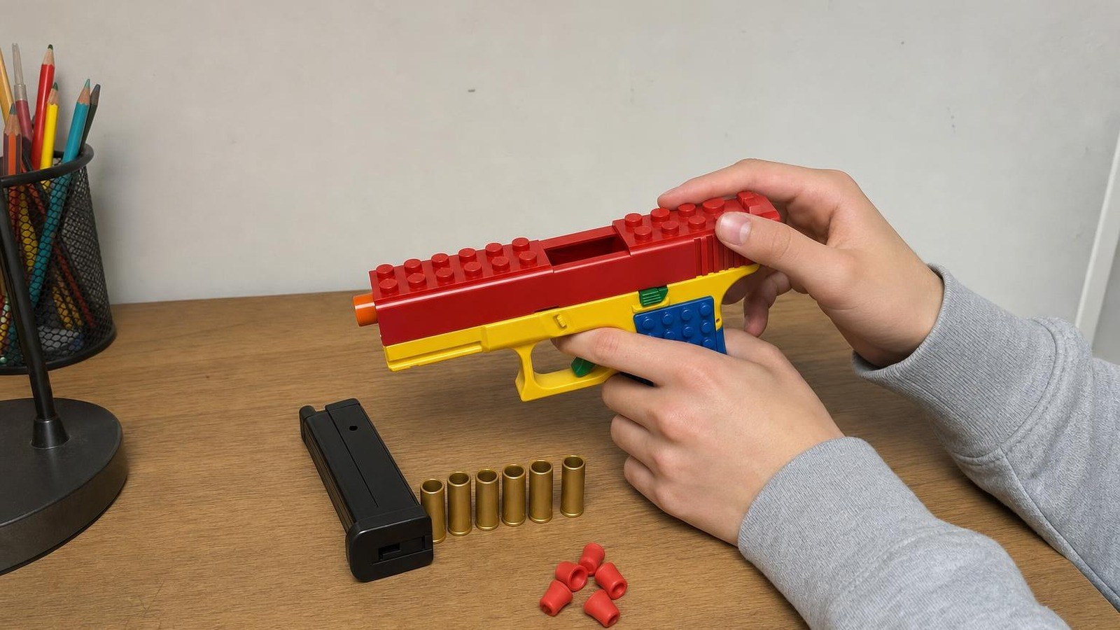 A teenager holds the BlockBlaster with the slide pulled back and the magazine out, empty casings and soft tips beside it