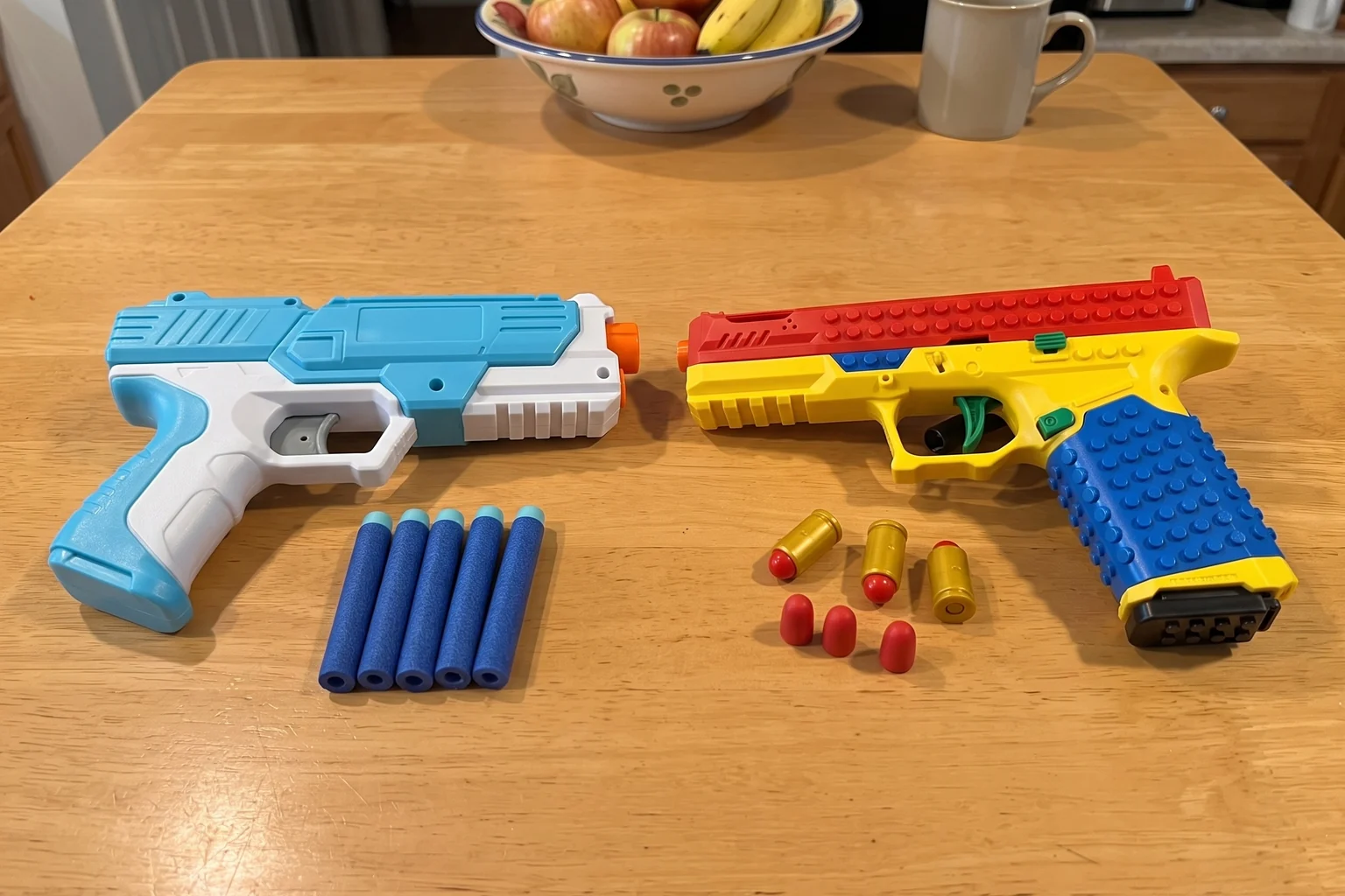 A standard foam dart blaster on the left and the brick-built BlockBlaster with its magazine and slide on the right, side by side on a kitchen table