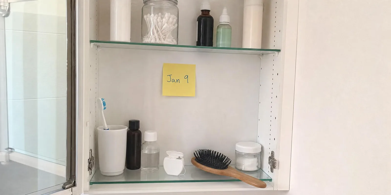 A handwritten date on a yellow sticky note inside an open bathroom medicine cabinet