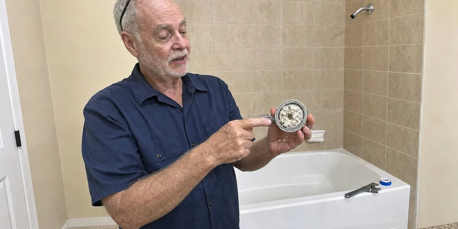 The plumber holding the unscrewed showerhead, packed with white crust