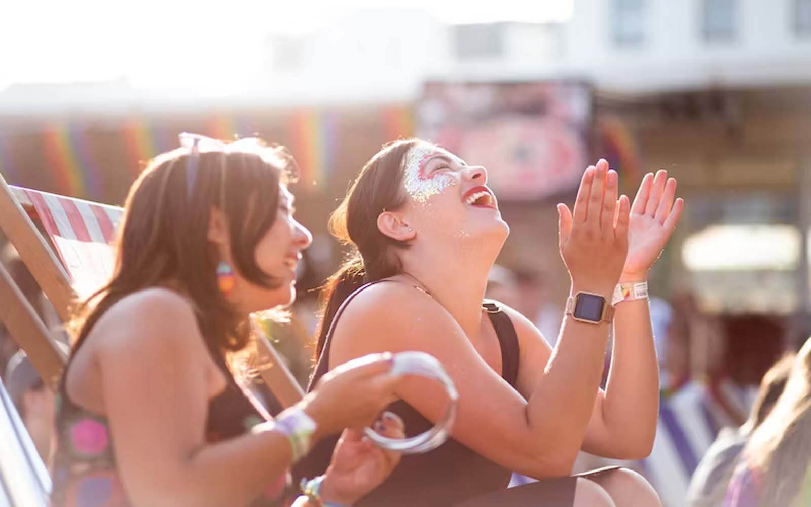 Two girls in dresses smile and clap their hands; one of them has glitter makeup on her face.