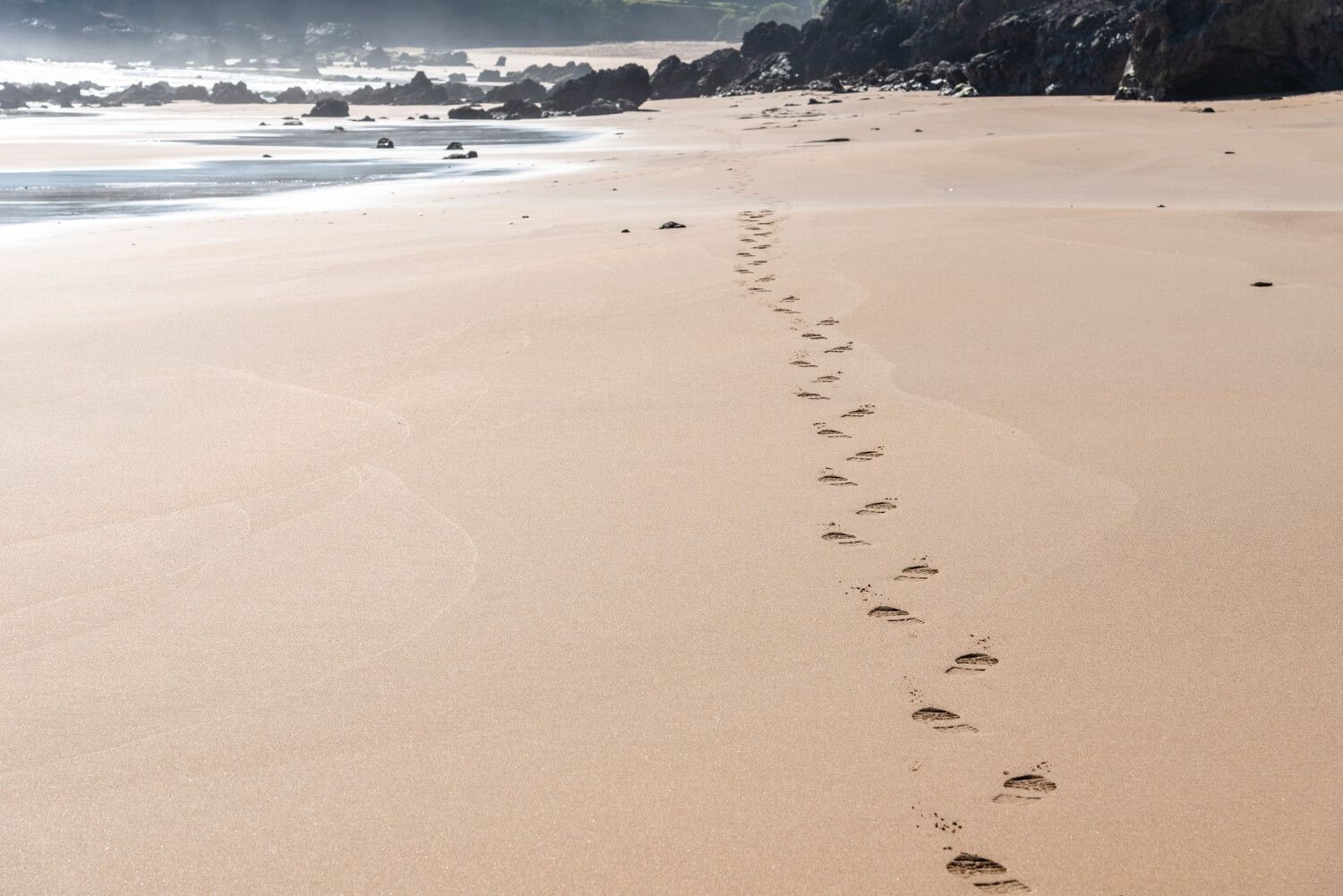 Footprints on sand with a pink ribbon nearby