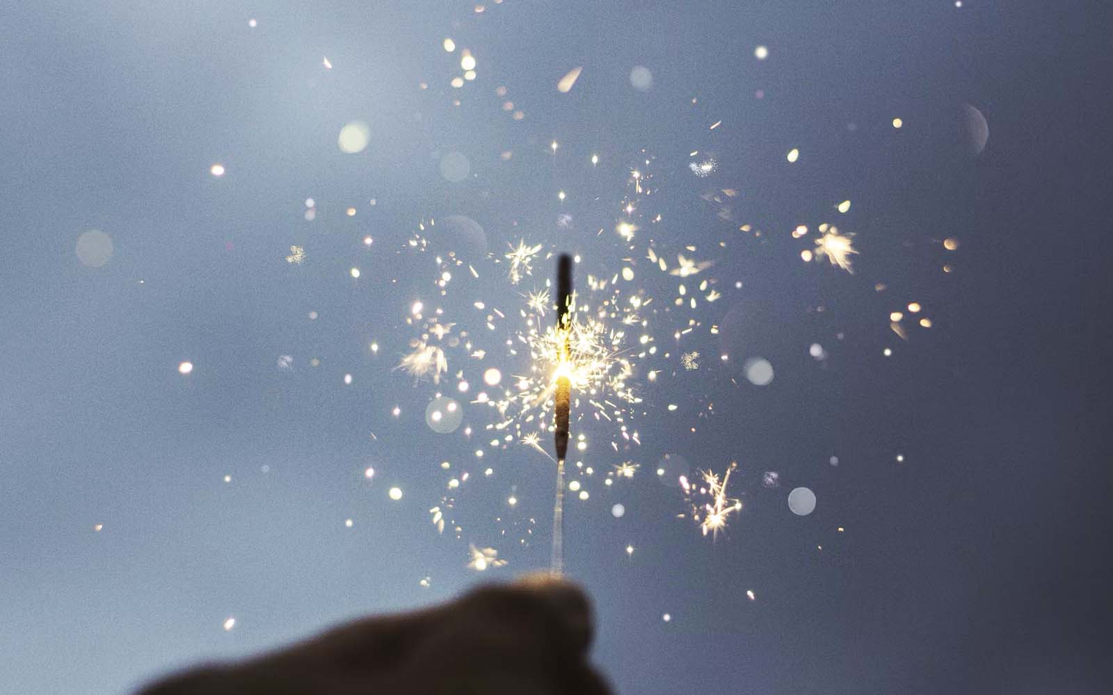 Hands holding a lit sparkler against the backdrop of the sky.