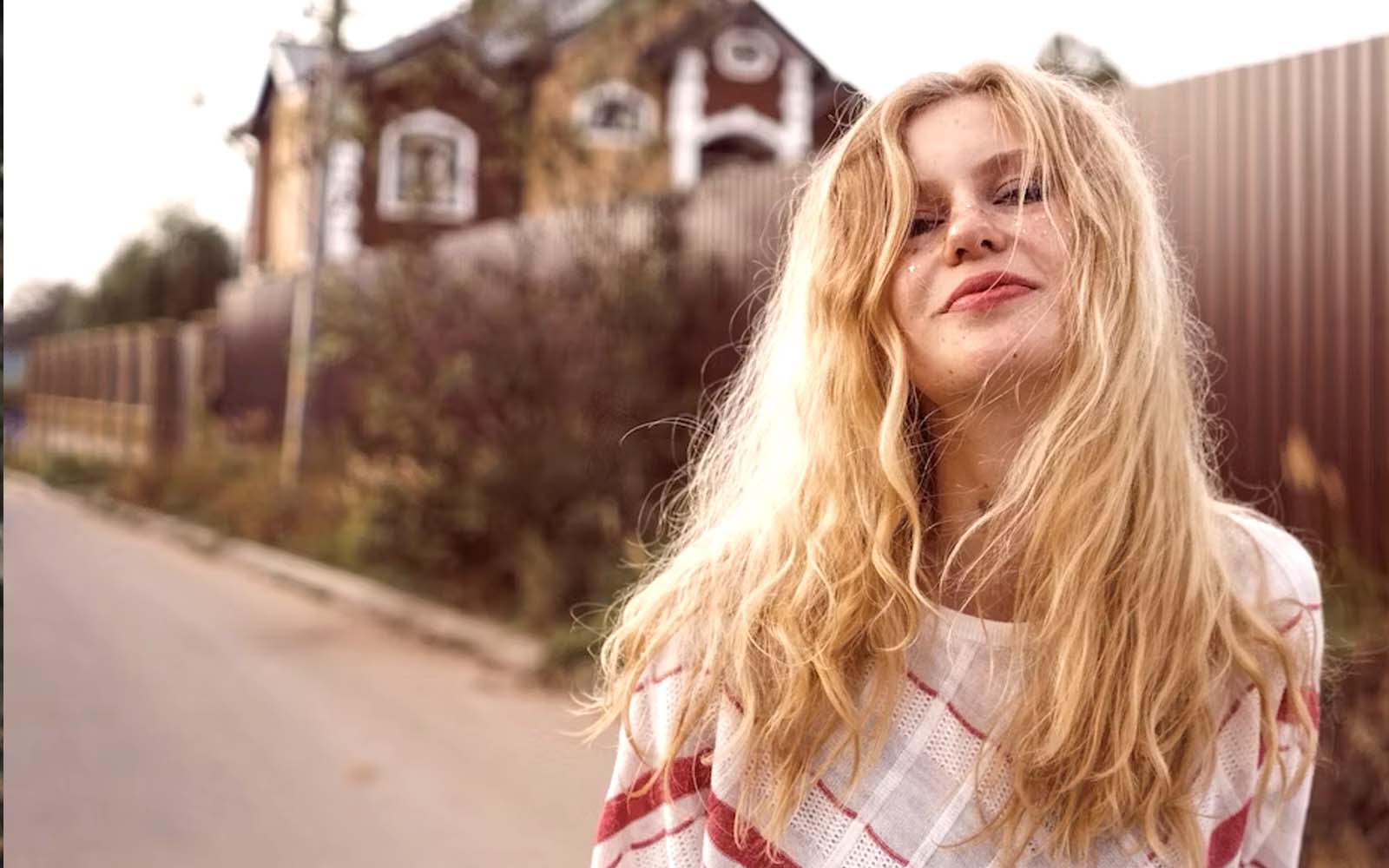 A beautiful girl poses in front of a house, her cheeks adorned with makeup in the form of glitter and stars.