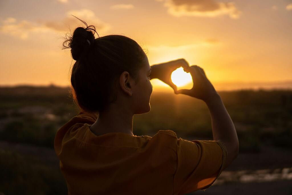 woman making a heart in front of the sunset