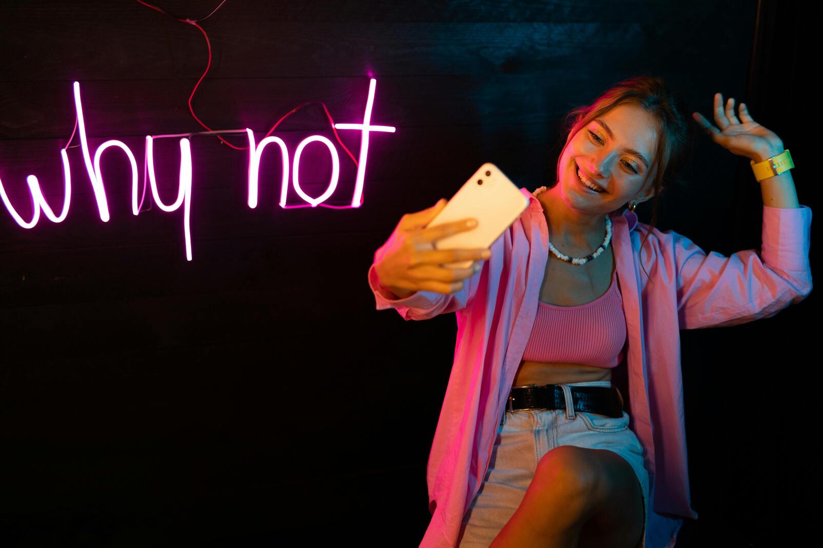 girl posing in front of neon sign taking a selfie