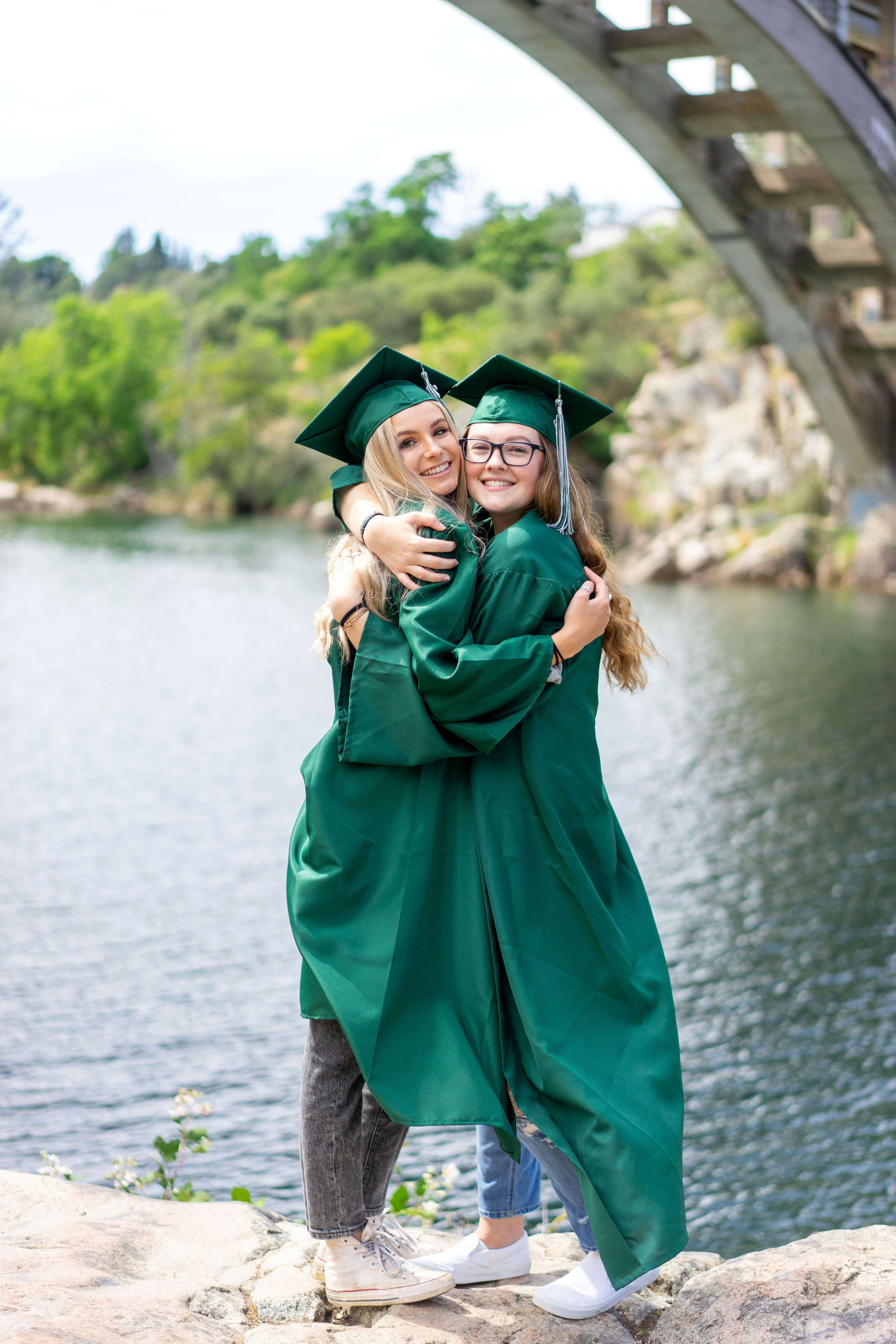 two girls hugging in graduation attire in front of a lake