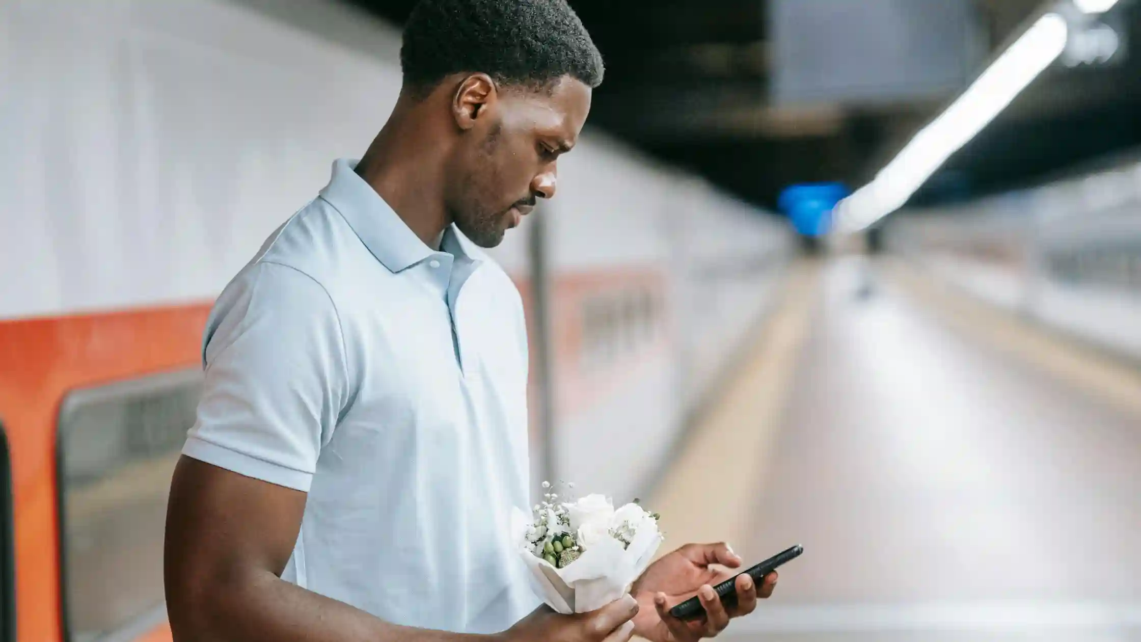 A man holding flowers while texting somebody on his phone.