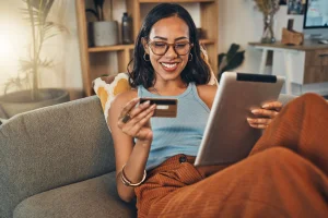 Smiling woman using credit card to buy a direct buy auto warranty on digital tablet at home