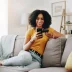 Attractive woman sitting on a sofa purchasing the best online car warranty on her phone