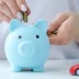 Hand putting coin in blue piggy bank next to toy red car saving money to buy a budget friendly warranty