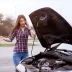 woman in a plaid shirt next to a broken down car with a warranty that has ended