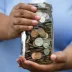 Man with blue shirt holding up a jar filled with coins