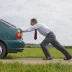man in a tie pushing a green compact car that has broken down