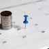 A blue tack and a pile of coins on a calendar signifying a monthly car warranty payment plan