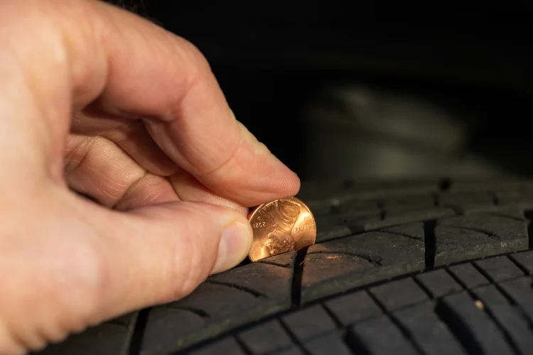 Driver performing a penny test on a tire to determine tread depth