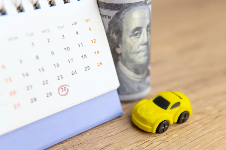 Photo illustration of a monthly car warranty payment with a calendar, roll of $100 bills, and a toy car