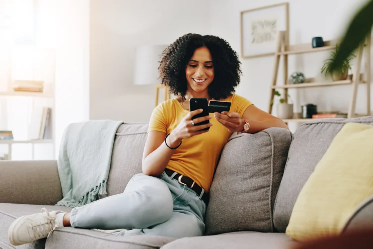 Attractive woman sitting on a sofa purchasing the best online car warranty on her phone
