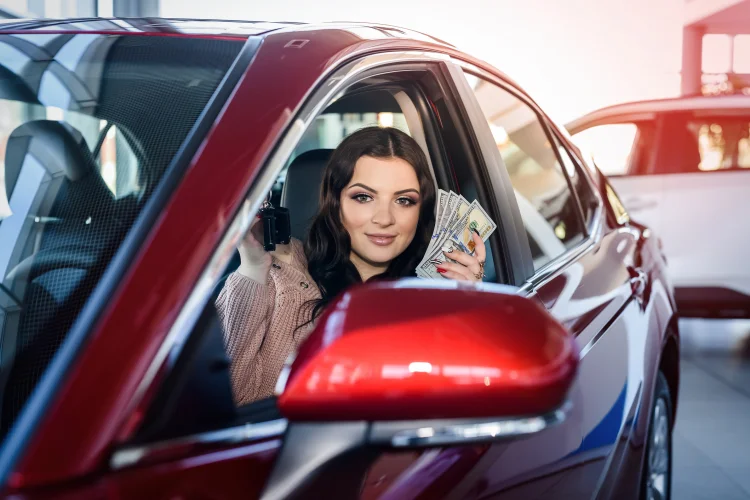 Woman sitting in a red car with a budget car warranty holding money and a car key