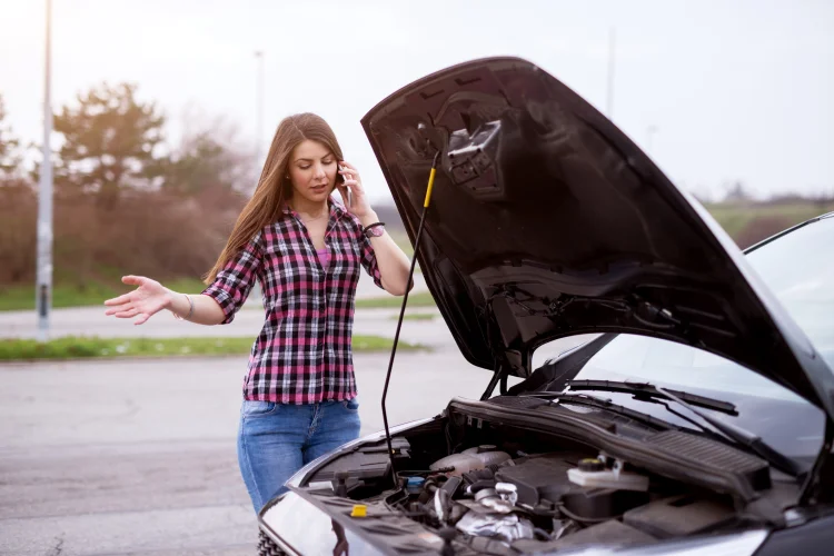 woman in a plaid shirt next to a broken down car with a warranty that has ended