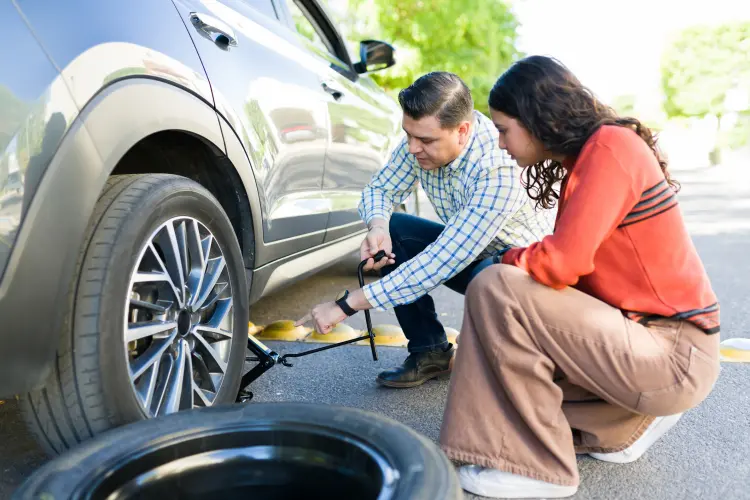 Person using a jack to lift a car and change a flat tire on the roadside