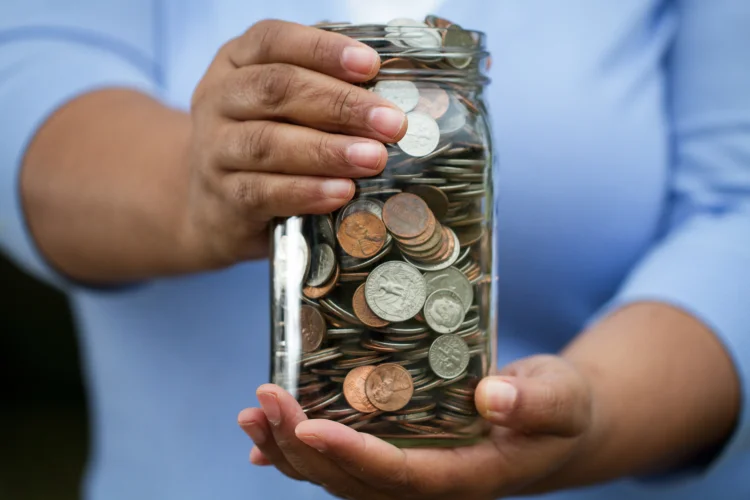 Man with blue shirt holding up a jar filled with coins