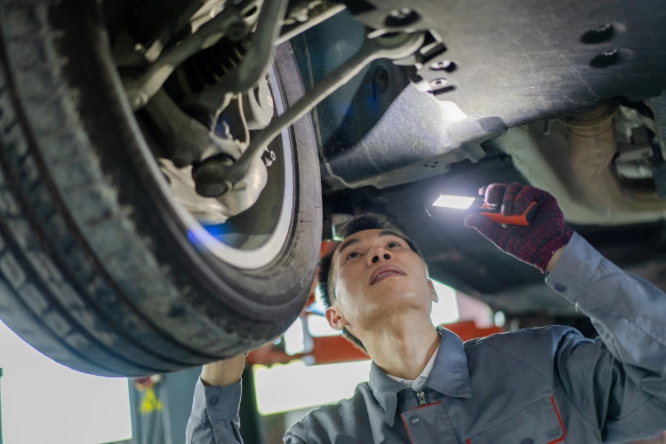 Auto mechanic using a flashlight to carefully inspect the underside of a vehicle in a professional garage setting