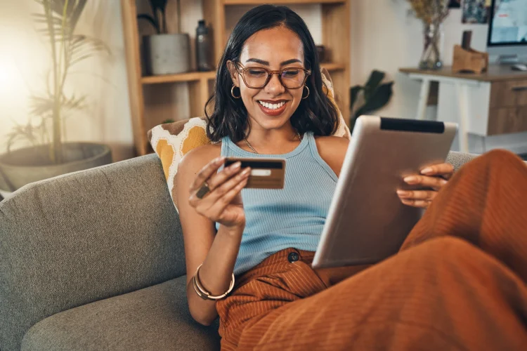 Smiling woman using credit card to buy a direct buy auto warranty on digital tablet at home