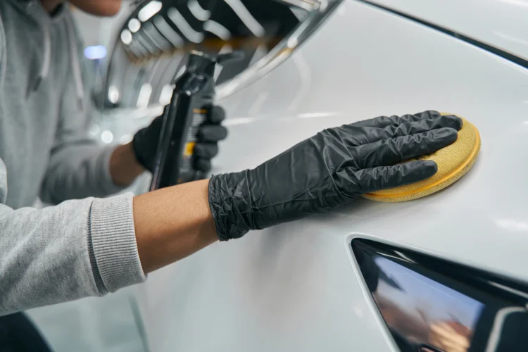 close up of a white car being waxed with a yellow sponge