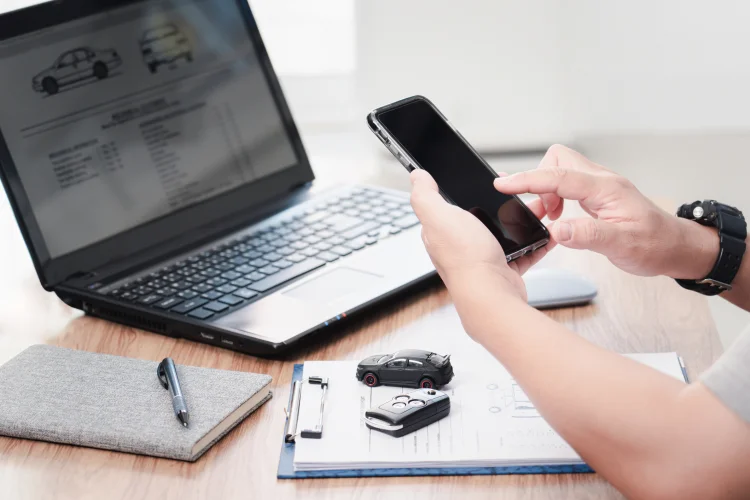 man holding a smartphone doing a lease buyout on his laptop