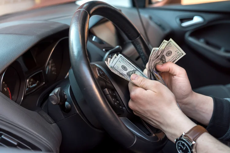 Man counting hundred dollar bills in car