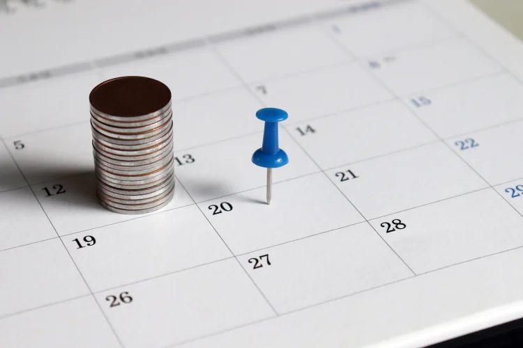 A blue tack and a pile of coins on a calendar signifying a monthly car warranty payment plan