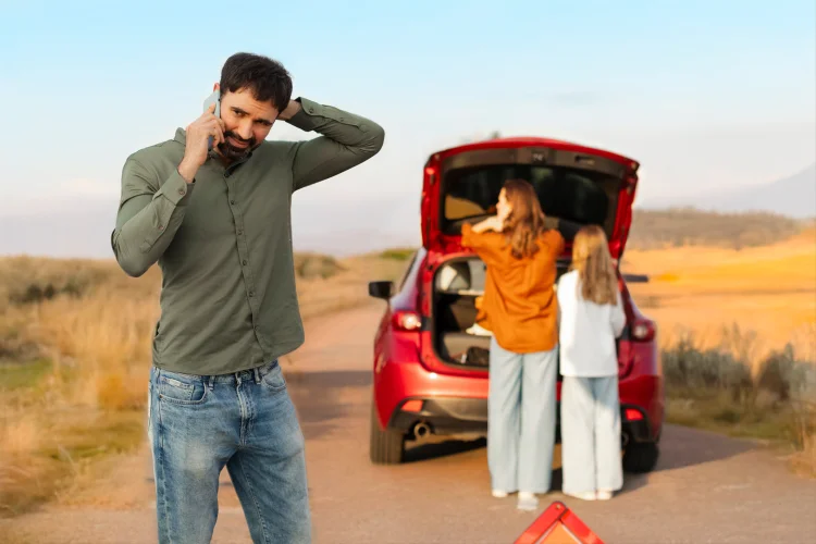 Man with powertrain warranty coverage on a cell phone in front of a broken down car red car with family on the way to vacation
