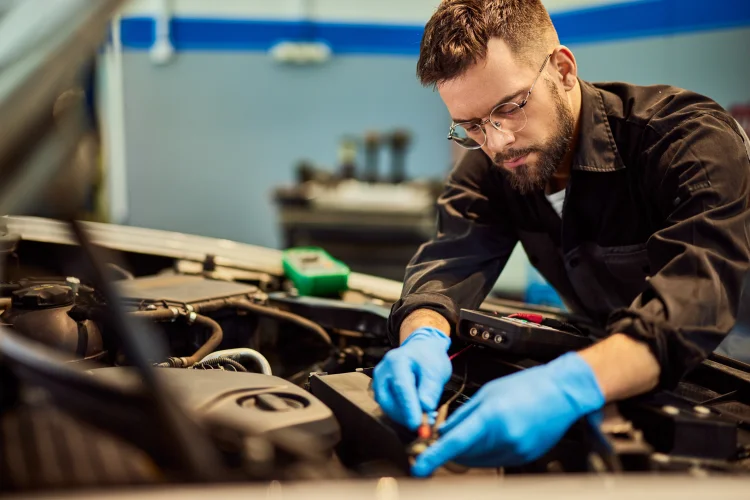 A male mechanic, fixing a car, and connecting cables