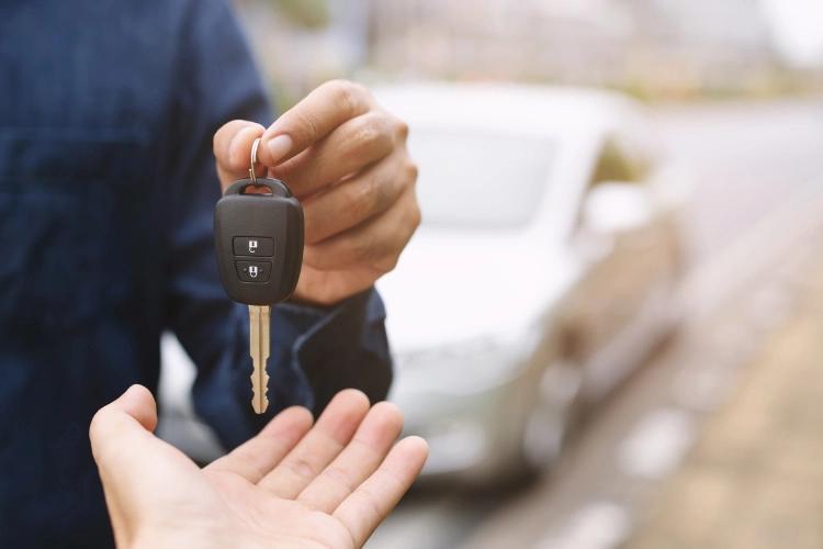 Close-up of a person handing over a car key after selling a vehicle, with a blurred car in the background.