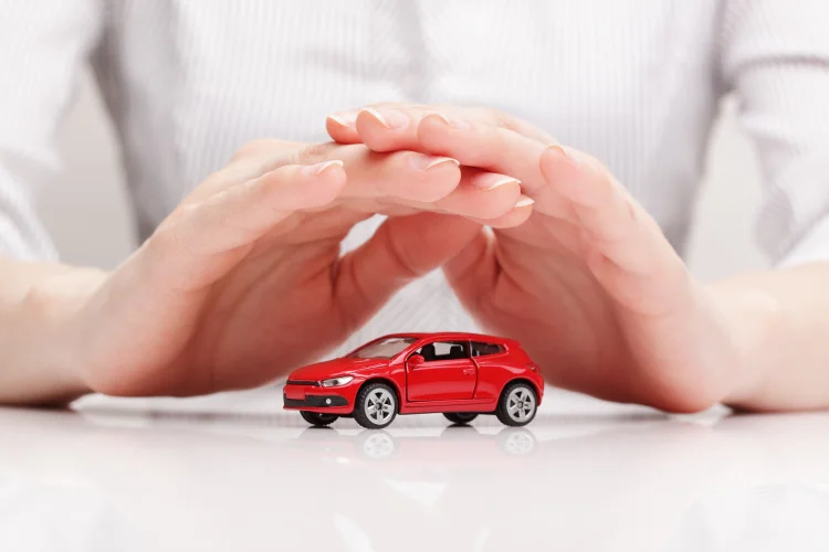 Red toy car shielded by interlocked hands representing a vsc car warranty
