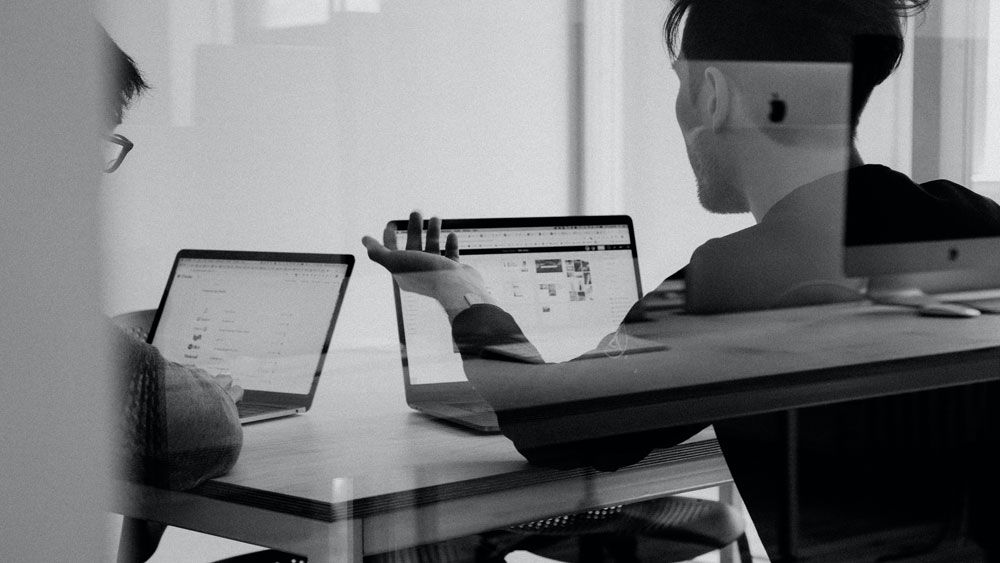 two men at a desk with their laptops