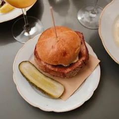 A Leberkäse bun with a pickle on a gold rimmed plate at Theke in Berlin