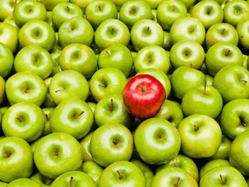 This picture shows a bushel of green apples and one red apple, which highlights the anomaly in the bunch.