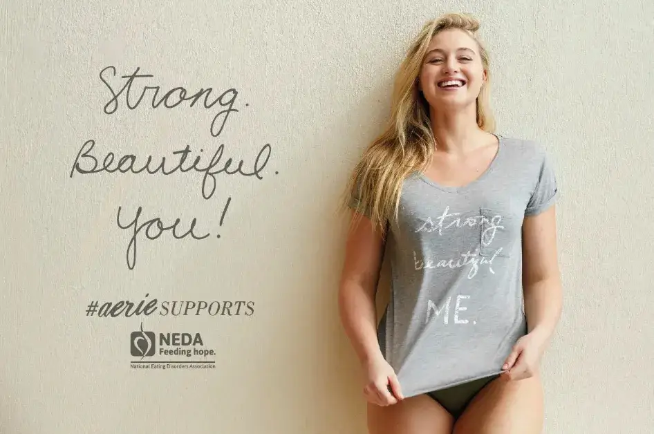 This image demonstrates smiling woman in a gray T-shirt reading "Strong. Beautiful. Me." Text beside her says "Strong. Beautiful. You!" with #aerieSUPPORTS and the NEDA logo, promoting self-acceptance.