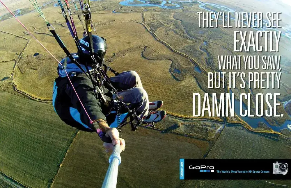 This image shows a paraglider taking a selfie with a GoPro, capturing panoramic views below. The text reads, 'They’ll never see exactly what you saw, but it’s pretty damn close'