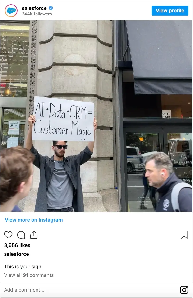 This image shows a man standing outside a building, holding a sign that reads, "AI + Data + CRM = Customer Magic." It is a screenshot from Salesforce's Instagram post with the caption, "This is your sign."