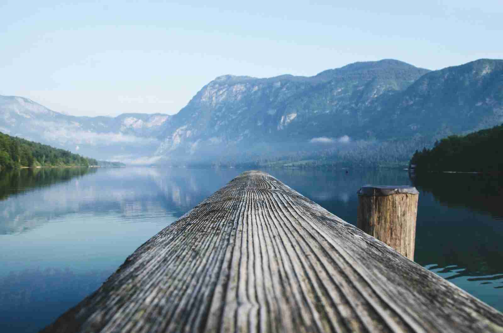 gray wood beam near body of water surrounded by mountain ranges during daytime