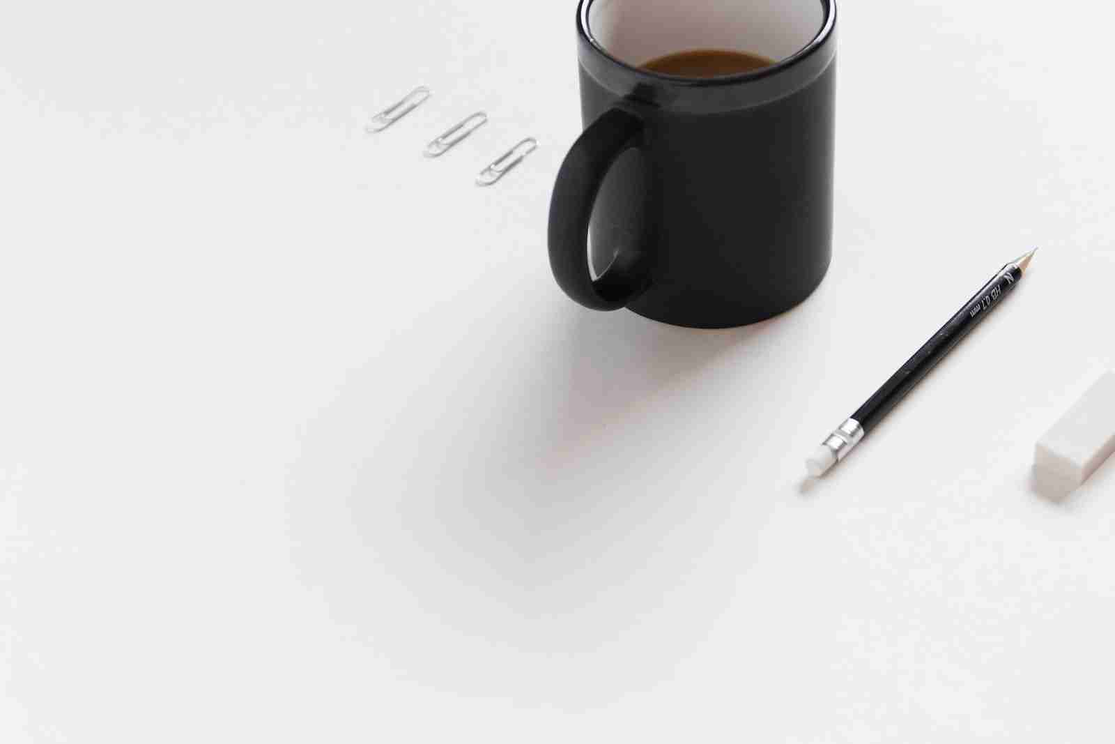 three white paper clips, black ceramic mug, black pencil, and white pencil eraser on white surface