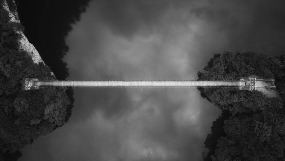 The Structural Link - Binding Perpetual Readiness to Permanent Value. An aerial monochrome view of a suspension bridge, symbolizing the DOUGLAS USA Operating System (OS). It serves as the single source of truth that binds philosophy, diagnostics, and methodology into a unified fortress of valuation certainty across the entire business lifecycle