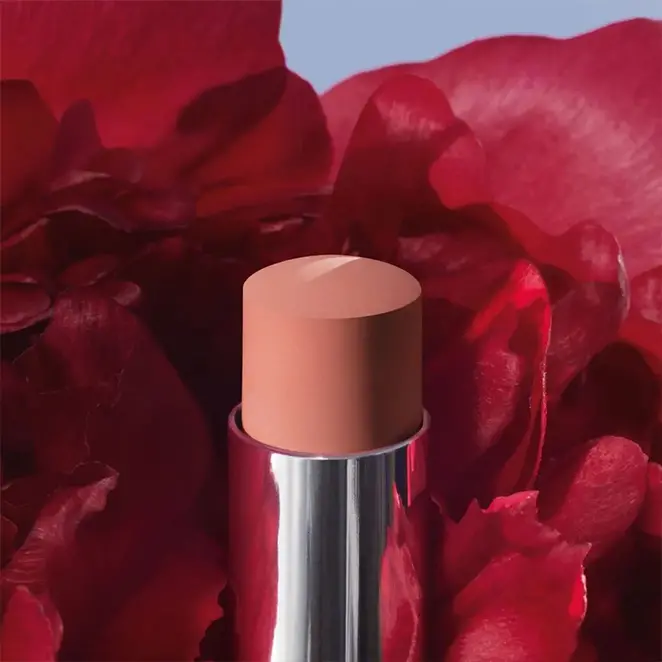 Tube de rouge à lèvres Dior teinte nude entouré de fleurs rouges.