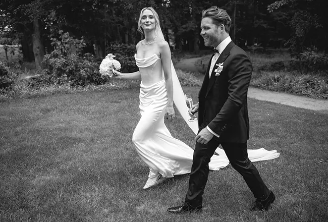 Mariée en tenue sobre et marié marchant ensemble en plein air, photo noir et blanc.