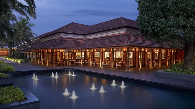Bâtiment traditionnel d’Alila Diwa Goa illuminé au crépuscule, bordé d’une piscine et de palmiers tropicaux.