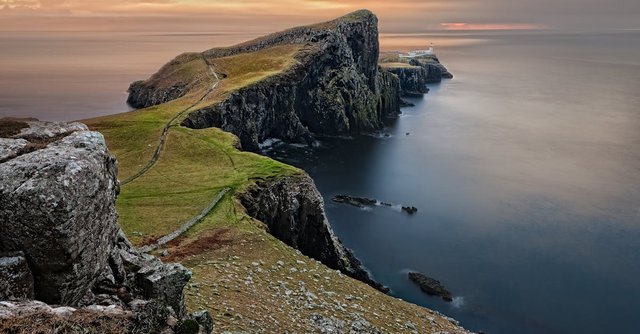 A stunning sunset view of Neist Point Lighthouse with cliffs and serene sea in Scotland.